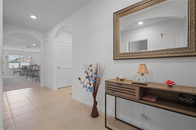 corridor with light tile patterned floors, baseboards, recessed lighting, and arched walkways