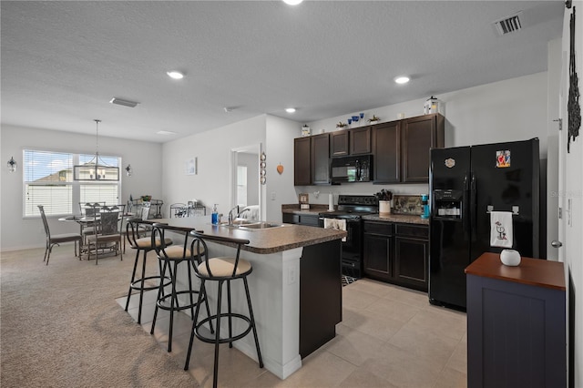 kitchen with visible vents, a sink, dark countertops, a kitchen bar, and black appliances