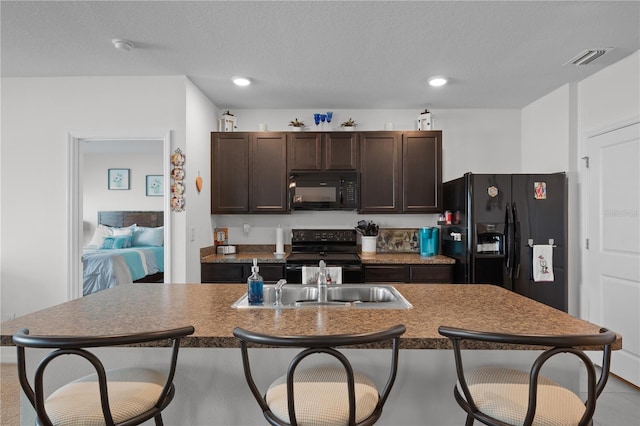 kitchen with a sink, black appliances, a breakfast bar, and dark brown cabinetry