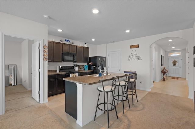 kitchen with light carpet, an island with sink, a breakfast bar area, arched walkways, and black appliances