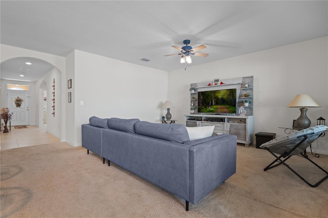 living area featuring baseboards, light carpet, a ceiling fan, visible vents, and arched walkways