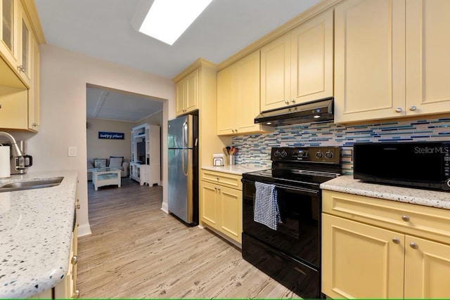 kitchen featuring black electric range oven, under cabinet range hood, cream cabinets, a sink, and freestanding refrigerator