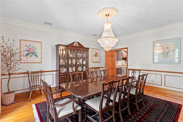 dining room with an inviting chandelier, wood finished floors, a wainscoted wall, and crown molding
