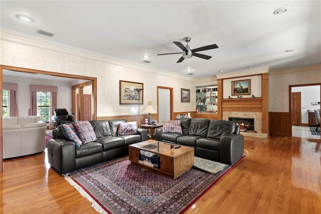 living room featuring a wainscoted wall, visible vents, light wood finished floors, ceiling fan, and crown molding