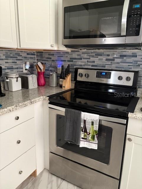 1408 San Juan Ct, Clearwater, FL 33756 - kitchen featuring appliances with stainless steel finishes, white cabinets, decorative backsplash, and light stone countertops