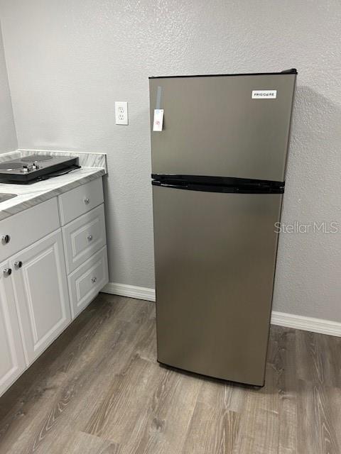 1408 San Juan Ct, Clearwater, FL 33756 - detailed view of freestanding refrigerator, wood finished floors, baseboards, and a textured wall