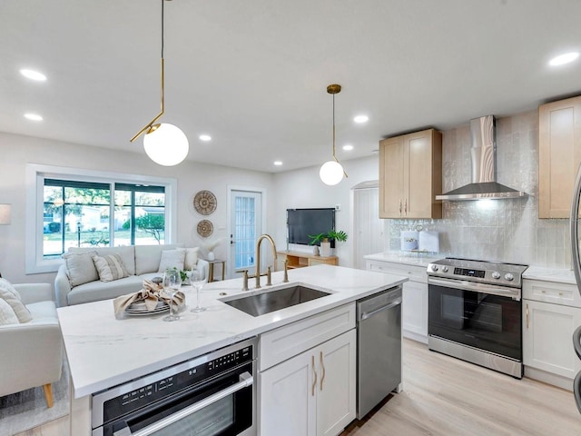 kitchen with open floor plan, stainless steel appliances, backsplash, a sink, and wall chimney range hood