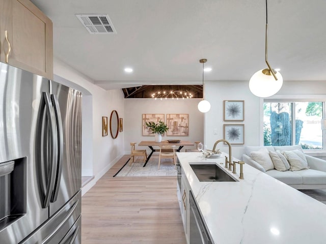 kitchen with light stone counters, a sink, light wood finished floors, appliances with stainless steel finishes, and visible vents