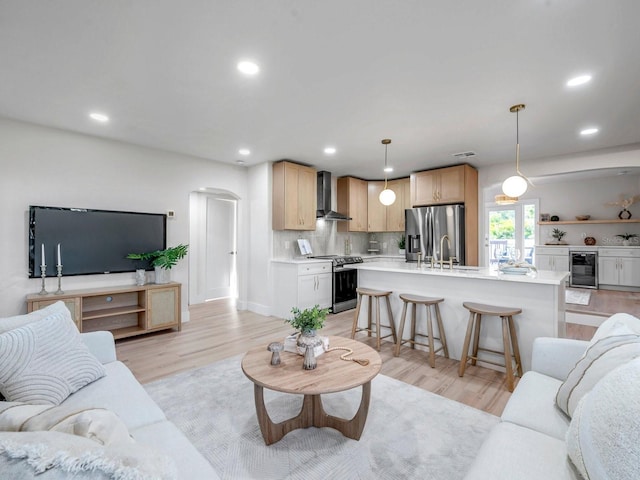 living room with light wood-style flooring, recessed lighting, arched walkways, and beverage cooler