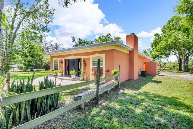 view of side of property with a chimney, a fenced front yard, central air condition unit, stucco siding, and a lawn