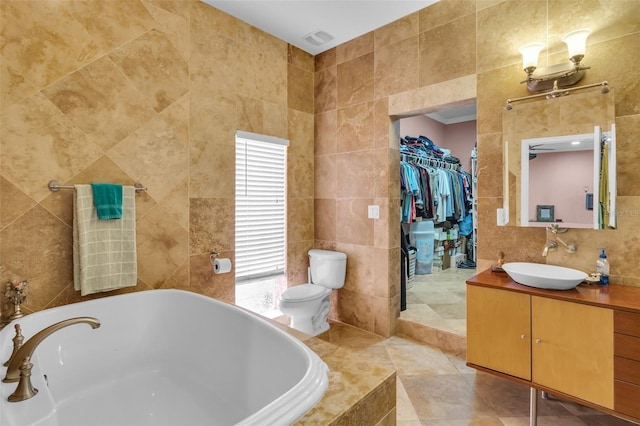 full bathroom featuring a walk in closet, tile walls, vanity, and a relaxing tiled tub