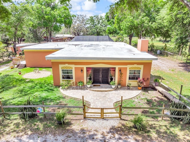 back of property featuring french doors, a fenced front yard, a chimney, a yard, and stucco siding