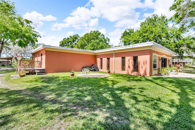 back of property with stucco siding, a wooden deck, a yard, and a patio