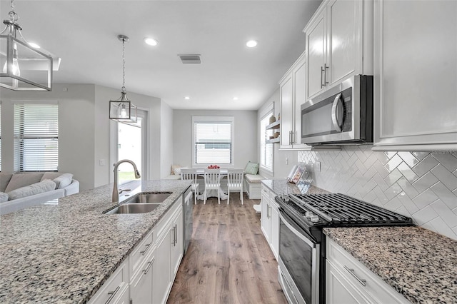 kitchen featuring visible vents, wood finished floors, appliances with stainless steel finishes, a sink, and backsplash