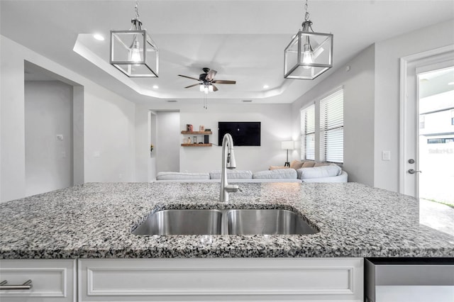 kitchen featuring a sink, a ceiling fan, a raised ceiling, light stone countertops, and open floor plan