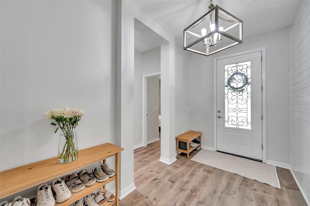entryway featuring baseboards, light wood-type flooring, and a notable chandelier
