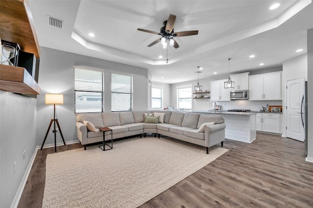 living room featuring visible vents, baseboards, ceiling fan, wood finished floors, and a raised ceiling