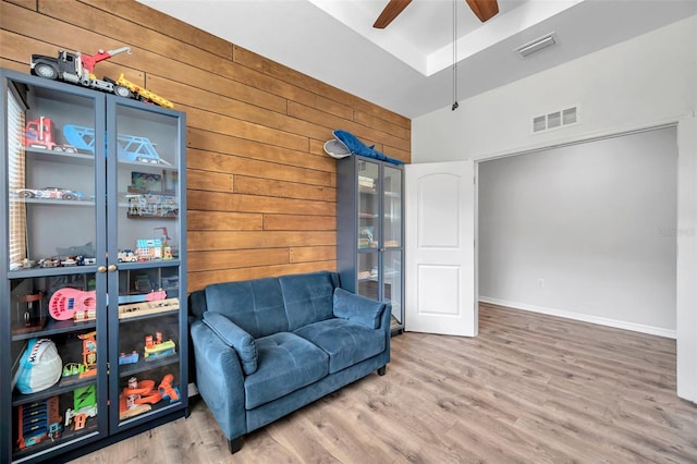 living area with wood walls, visible vents, a ceiling fan, and wood finished floors