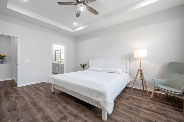 bedroom featuring a tray ceiling, connected bathroom, dark wood-style floors, baseboards, and recessed lighting