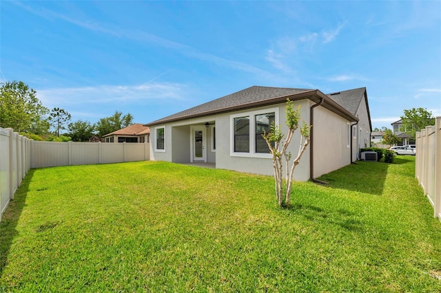 rear view of house featuring a fenced backyard, roof with shingles, stucco siding, and a yard