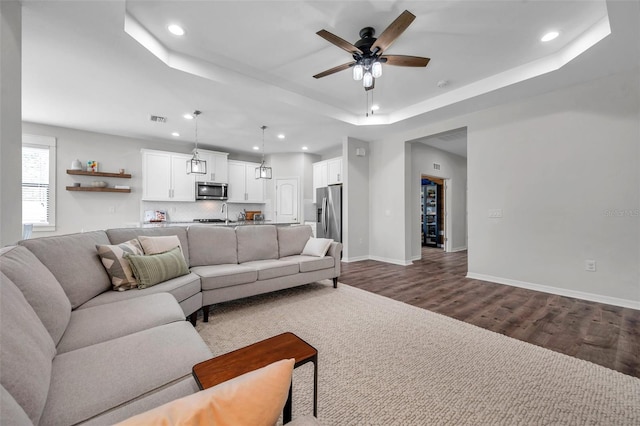 living room featuring dark wood-style flooring, visible vents, ceiling fan, recessed lighting, and a tray ceiling