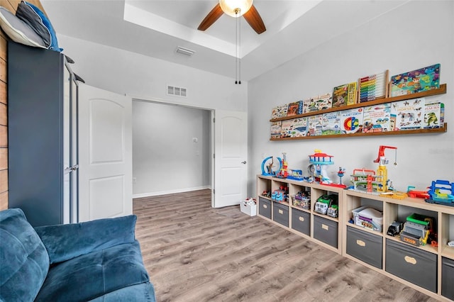 rec room featuring a ceiling fan, a raised ceiling, wood finished floors, and visible vents