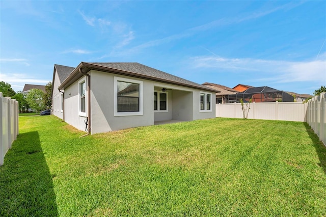 rear view of house featuring a fenced backyard, a lawn, stucco siding, and ceiling fan