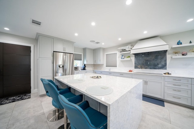 3986 Bennett Ln, Bonita Springs, FL 34134 - kitchen with visible vents, custom exhaust hood, a kitchen island, open shelves, and stainless steel fridge with ice dispenser