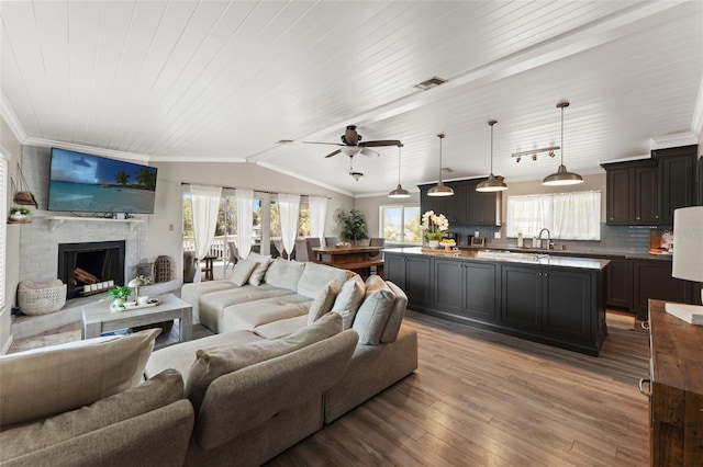 living room featuring lofted ceiling, visible vents, light wood-type flooring, and crown molding