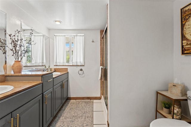 full bathroom featuring a shower stall, baseboards, double vanity, a sink, and tile patterned flooring