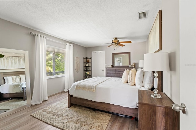 bedroom featuring wood finished floors, a textured ceiling, ceiling fan, and visible vents