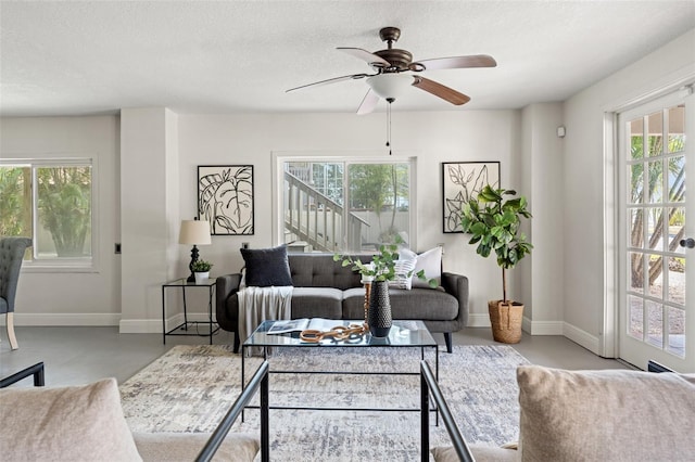 living room with baseboards, a ceiling fan, a textured ceiling, and a healthy amount of sunlight