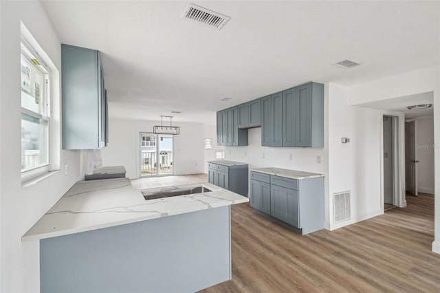 15621 Bertram Dr, Hudson, FL 34667 - kitchen featuring light stone counters, light wood-style floors, gray cabinetry, a sink, and baseboards