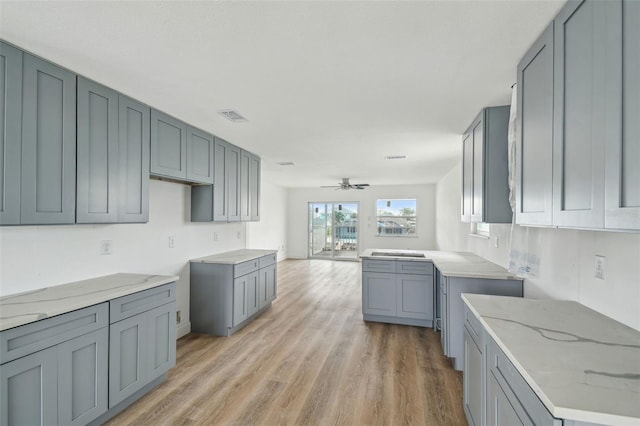 15621 Bertram Dr, Hudson, FL 34667 - kitchen featuring light stone counters, light wood finished floors, a ceiling fan, and gray cabinetry