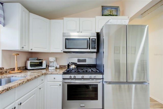 921 24th Ave N, Saint Petersburg, FL 33704 - kitchen with appliances with stainless steel finishes, light stone counters, white cabinets, lofted ceiling, and light wood finished floors