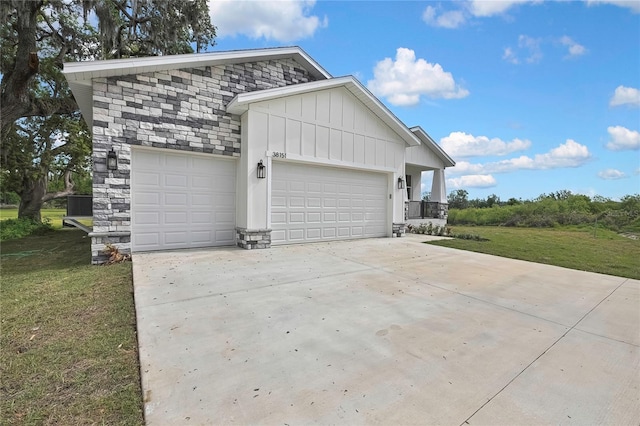 exterior space featuring driveway, stone siding, an attached garage, board and batten siding, and a lawn