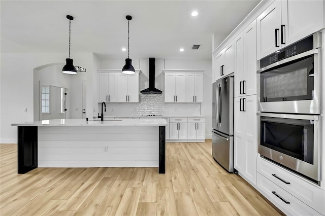 kitchen with light countertops, a sink, wall chimney exhaust hood, stainless steel appliances, and decorative backsplash