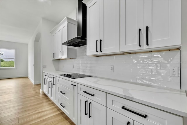 kitchen featuring white cabinetry, black electric cooktop, backsplash, wall chimney range hood, and light wood-style flooring
