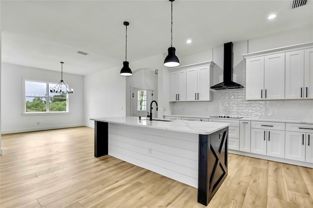 kitchen with decorative backsplash, visible vents, a sink, an island with sink, and wall chimney range hood