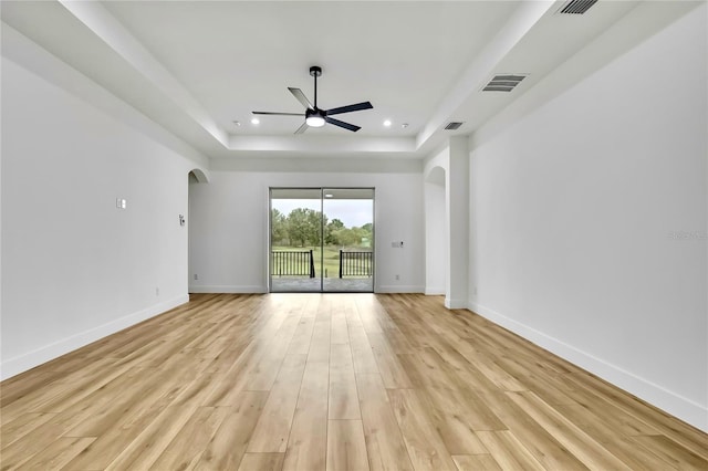 unfurnished room with arched walkways, a tray ceiling, baseboards, and ceiling fan