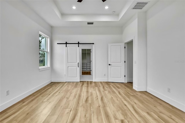 unfurnished bedroom with a raised ceiling, a barn door, and visible vents