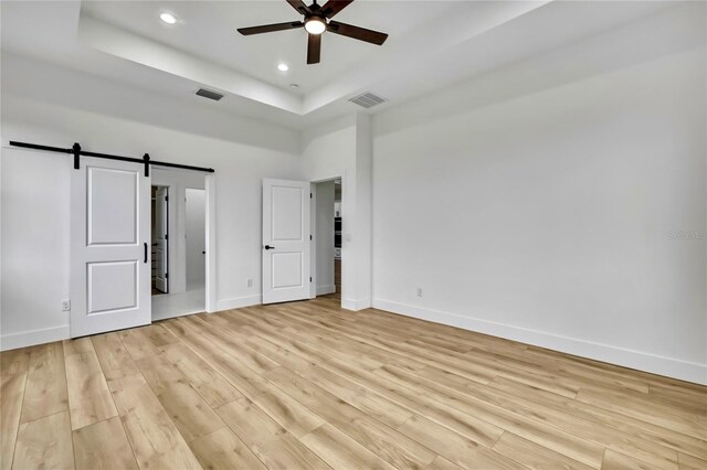 unfurnished bedroom with a tray ceiling, baseboards, visible vents, and light wood-style floors