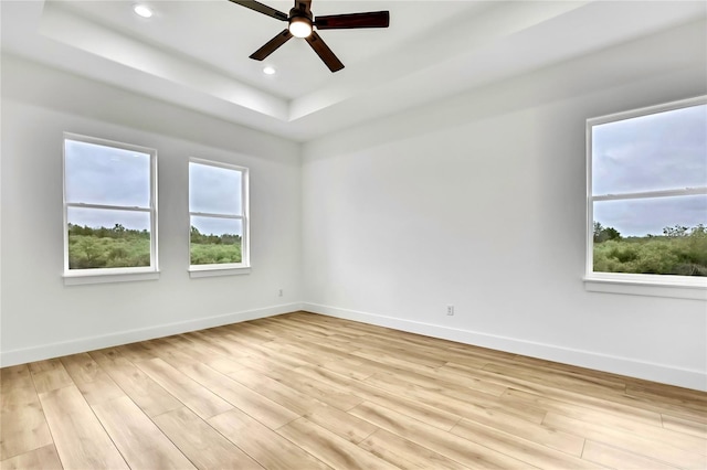 spare room with baseboards, a raised ceiling, a ceiling fan, and light wood finished floors