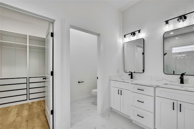 bathroom featuring marble finish floor, a sink, toilet, and double vanity
