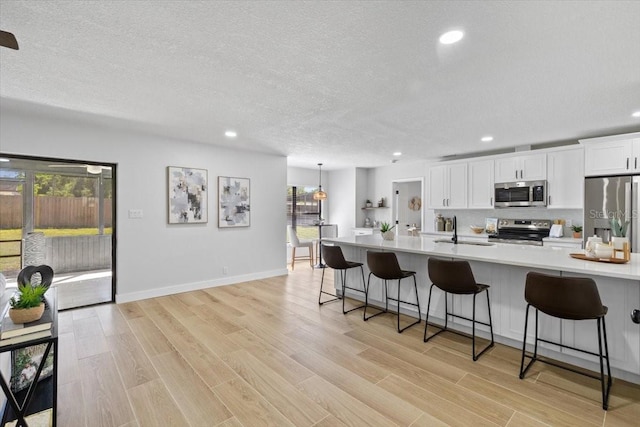 kitchen with white cabinetry, a breakfast bar, light countertops, a sink, and stainless steel appliances