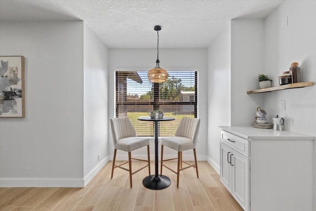 dining area with baseboards, light wood finished floors, and a textured ceiling