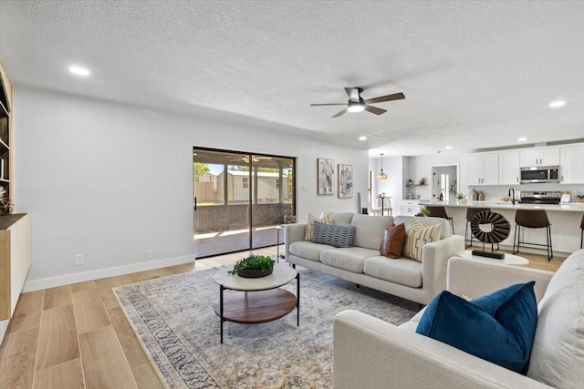 living area with light wood finished floors, a textured ceiling, ceiling fan, and recessed lighting