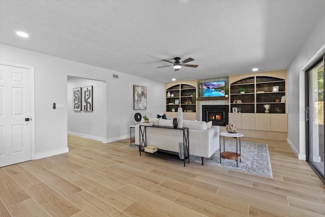 living room with a ceiling fan, light wood-style floors, and a textured ceiling