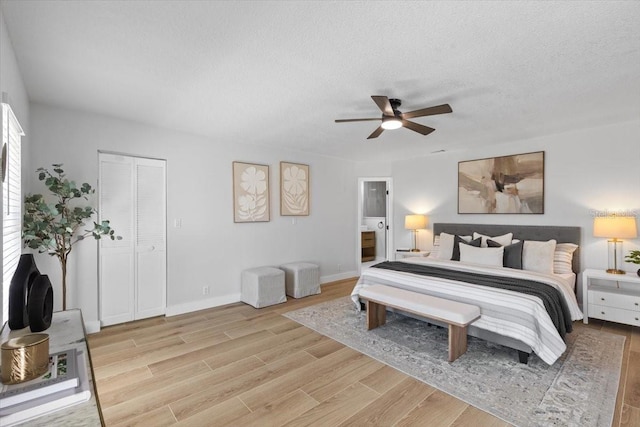 bedroom featuring ceiling fan, light wood-type flooring, a textured ceiling, ensuite bath, and baseboards
