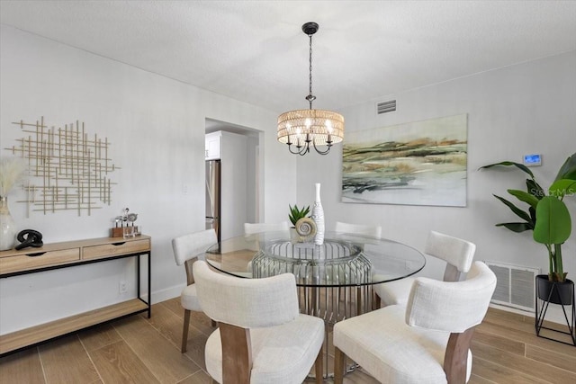 dining room featuring wood finished floors, a notable chandelier, and visible vents